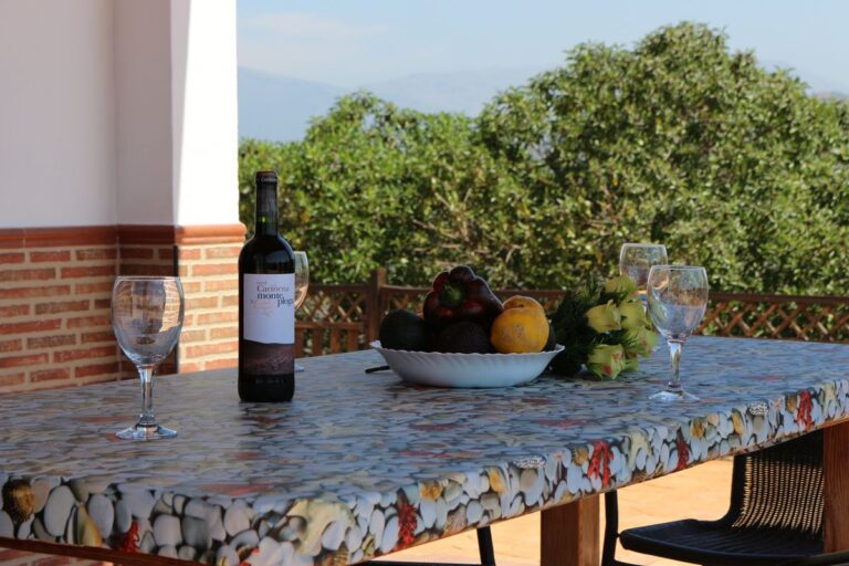 Mesa de piedra y madera con botella de vino, copas y frutero, en porche de casa rural